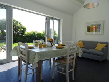 A dining area with a table set for four and a gray sofa with yellow cushions at The Studio in Rinsey Cove near Praa Sands