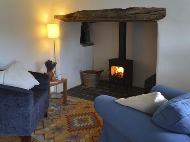 A living room with two armchairs a wood stove and a floor lamp at The Studio Rinsey Cove near Praa Sands