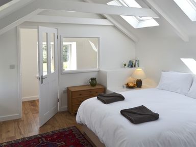 A bedroom with a white bed brown towels wooden chest of drawers lamp and skylights at The Studio Rinsey Cove near Praa Sands