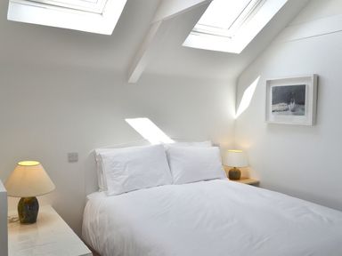 A bedroom with a double bed two lamps on side tables and skylight windows above at The Studio in Rinsey Cove near Praa Sands