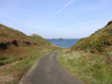 A narrow road between grassy hills leading to the sea with small rocky islands in the water at Mollys Cottage in St Just