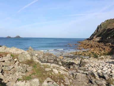 A rocky shoreline with the ocean and hills in the background at Mollys Cottage in St Just
