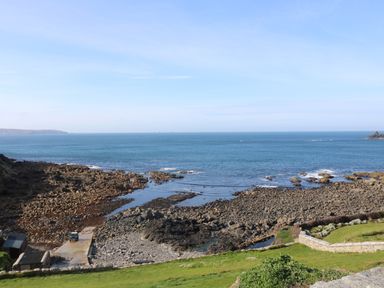 A rocky coastline with a pier and small buildings beside the sea at Mollys Cottage in St Just