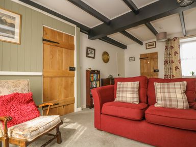 A living room with a red sofa and plaid cushions next to wooden doors and a wooden chair with a red cushion at Mollys Cottage in St Just