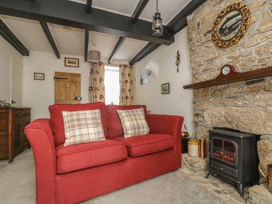 A living room with a red sofa and plaid cushions a stone fireplace with a clock and a mirror at Mollys Cottage in St Just