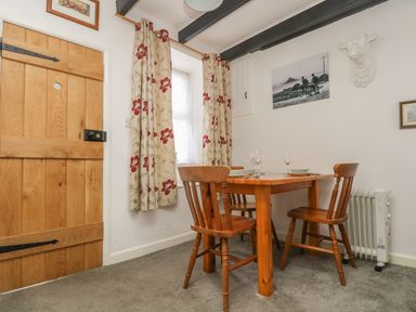 A dining area with a wooden table and three chairs near a window with floral curtains at Mollys Cottage in St Just