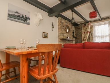 A dining table with wooden chairs and a red sofa in a room with stone walls and a window at Mollys Cottage in St Just
