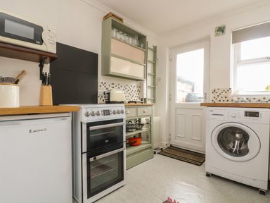 A kitchen with a stove fridge washing machine and storage shelves at Mollys Cottage in St Just