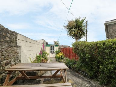 A garden with a wooden picnic table bushes flowers a small shed and a palm tree at Mollys Cottage in St Just