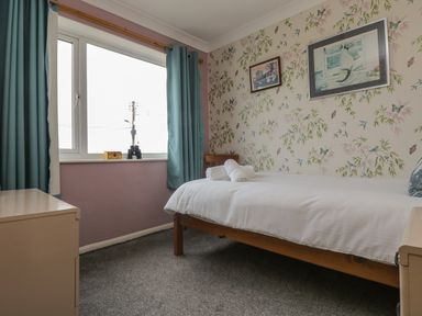 A bedroom with a single bed towels on it floral wallpaper and blue curtains at Mollys Cottage in St Just