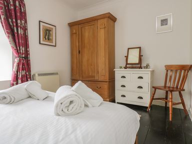 A bedroom with a bed rolled white towels a wooden chair a white dresser with a mirror and a wooden wardrobe at Mollys Cottage in St Just