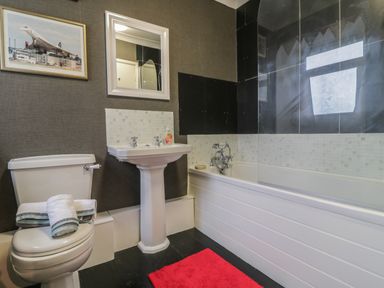 A bathroom with a toilet, sink, bathtub, mirror, and a picture of an airplane at Mollys Cottage in St Just