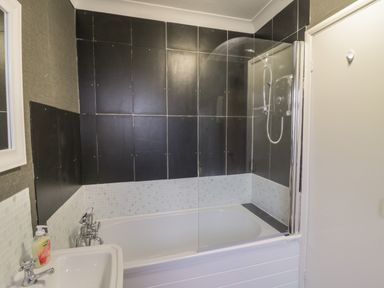 A bathroom with a bathtub white sink and black and white tiled walls at Mollys Cottage in St Just