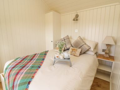 A bedroom with a bed featuring pillows and a plaid blanket a bedside table with a lamp and a tea set on a tray at Hillside View in Rhayader