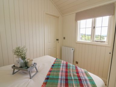 A bedroom with a bed a multicolored blanket a tray with a vase and cups a door and a window at Hillside View in Rhayader