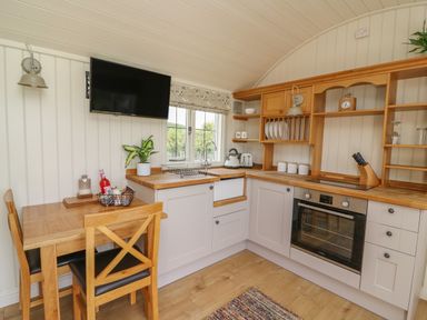 A kitchen with wooden cabinets a table and chairs a wall mounted television and a window at Hillside View in Rhayader