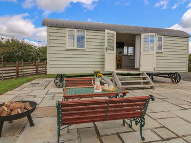 An outdoor patio with wooden benches and a metal table in front of a small building on wheels at Hillside View in Rhayader