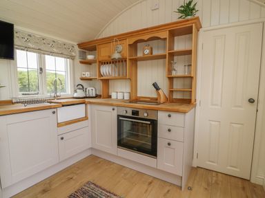 A kitchen with white cabinets wooden countertops an oven a window and shelves at Hillside View in Rhayader