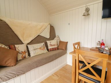 A corner with a cushioned bench with animal print pillows and a wooden dining table with chairs at Hillside View Rhayader