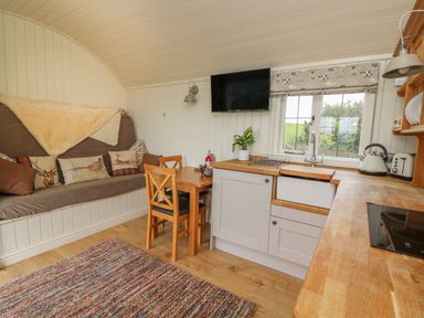 A kitchen with wooden countertops a table two chairs a bench with cushions a wall mounted television and a window at Hillside View in Rhayader
