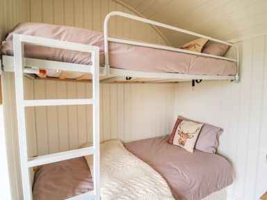 A bunk bed with a white metal frame and purple bedding in a room with white paneled walls at Hillside View in Rhayader