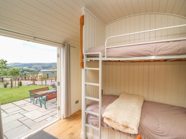 A small bedroom with bunk beds and an open door leading to a patio with a table and bench outside at Hillside View in Rhayader