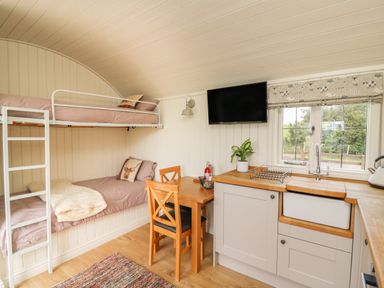 A small room with bunk beds a wooden table with two chairs a kitchen sink and a wall mounted TV at Hillside View in Rhayader
