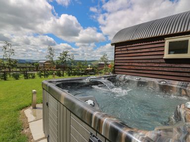 An outdoor hot tub with water flowing next to a wooden building under a partly cloudy sky at Woodland View in Rhayader