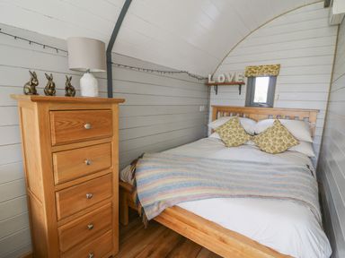 A bedroom with a wooden bed and chest of drawers with a lamp and rabbit figurines at Woodland View in Rhayader