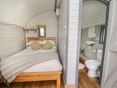 A bedroom with a wooden bed and patterned pillows next to a bathroom with a toilet and sink at Woodland View in Rhayader