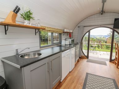 A kitchen with grey cabinets a black countertop a sink and appliances by a round glass door at Woodland View in Rhayader