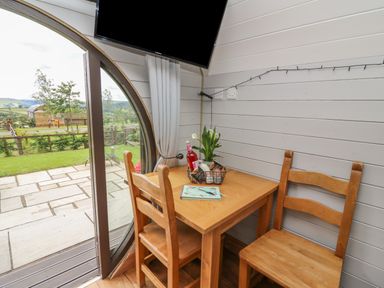 A small wooden dining table with two chairs near a round glass door and a mounted TV at Woodland View in Rhayader