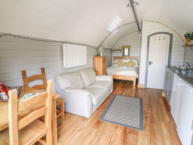A small living area with a wooden dining table and chairs a white sofa a wooden bed chest of drawers and a kitchen area in a pod style room at Woodland View in Rhayader