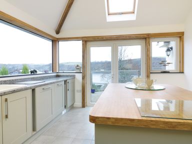 A kitchen with cabinets and a wooden countertop next to large windows and glass doors at Treetops Golant near Fowey