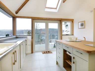 A kitchen with cabinets an island and glass doors leading to a balcony at Treetops Golant near Fowey