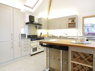 A kitchen with a wooden island, bar stools, cabinets, stove, and a window at Treetops in Golant near Fowey