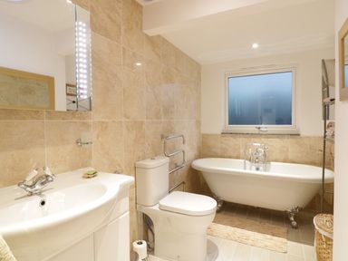 A bathroom with a sink, toilet, clawfoot bathtub, window, and mirrors at Treetops in Golant near Fowey
