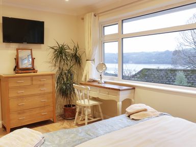 A bedroom with a dresser a chair a desk and a large window showing a water view at Treetops in Golant near Fowey