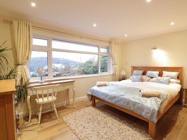 A bedroom with a wooden bed white desk and chair near a large window at Treetops in Golant near Fowey