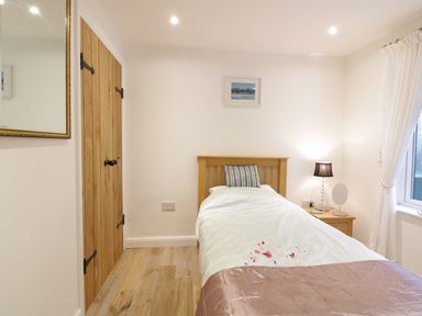 A bedroom with a single bed a wooden wardrobe a bedside table with a lamp and a window with curtains at Treetops in Golant near Fowey