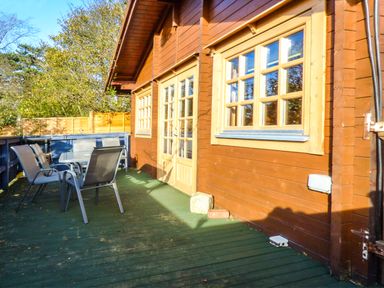 An outdoor wooden deck with a table and chairs beside a wooden building with windows at St Hildas Lodge in Hinderwell near Runswick Bay
