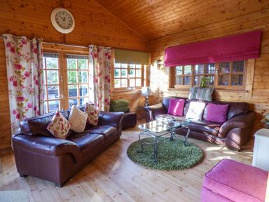 A wooden living room with two brown leather sofas pink and floral cushions glass coffee table and floral curtains at St Hilda's Lodge in Hinderwell near Runswick Bay