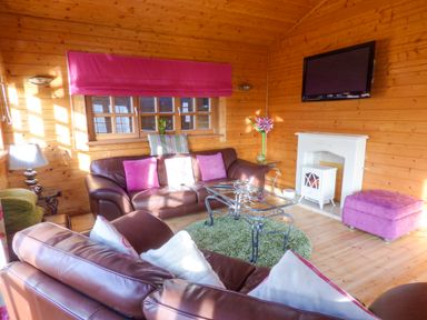 A wooden living room with brown leather sofas pink cushions a glass coffee table and a wall-mounted TV at St Hildas Lodge in Hinderwell near Runswick Bay