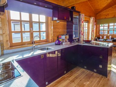 A kitchen with purple cabinets wooden walls and windows at St Hildas Lodge Hinderwell near Runswick Bay