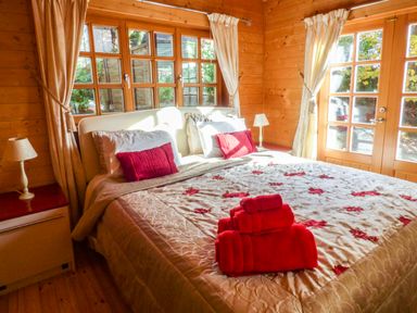 A bedroom with a bed red pillows folded towels bedside table lamps and wooden walls at St Hilda's Lodge in Hinderwell near Runswick Bay
