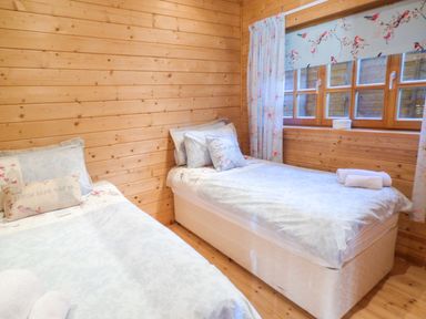 A bedroom with two single beds wooden walls and a window with floral curtains at St Hildas Lodge in Hinderwell near Runswick Bay