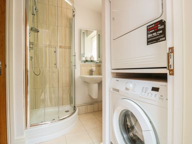 A bathroom with a glass shower enclosure a wall-mounted sink and a stacked washer and dryer at 33 Crescent Gardens in Bath