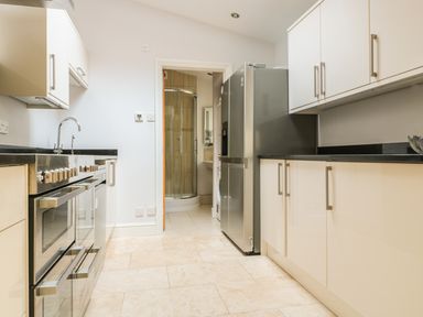 A kitchen with white cabinets black countertops a stainless steel refrigerator and an oven at 33 Crescent Gardens in Bath