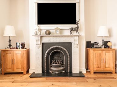 A fireplace with a white mantle and firewood surrounded by two wooden cabinets each with a lamp on top at 33 Crescent Gardens in Bath