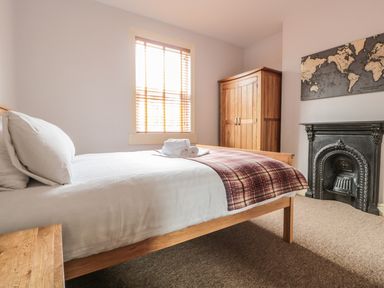 A bedroom with a bed with white sheets and plaid blanket a wooden wardrobe a map above a fireplace and a window with wooden blinds at 33 Crescent Gardens in Bath